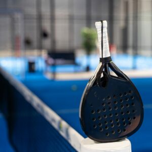 Paddle tennis: Padel racket and ball in front of an outdoor court.